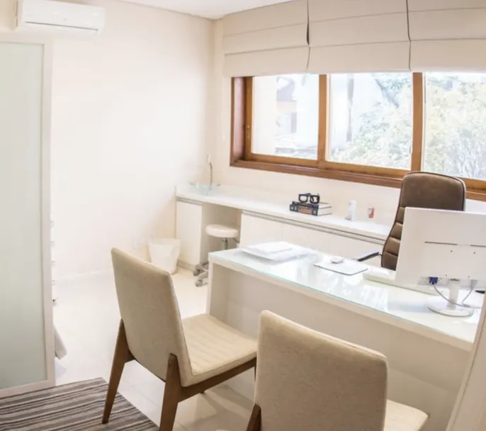 Sala de atendimento do consultório com mesa, computador e cadeiras para pacientes